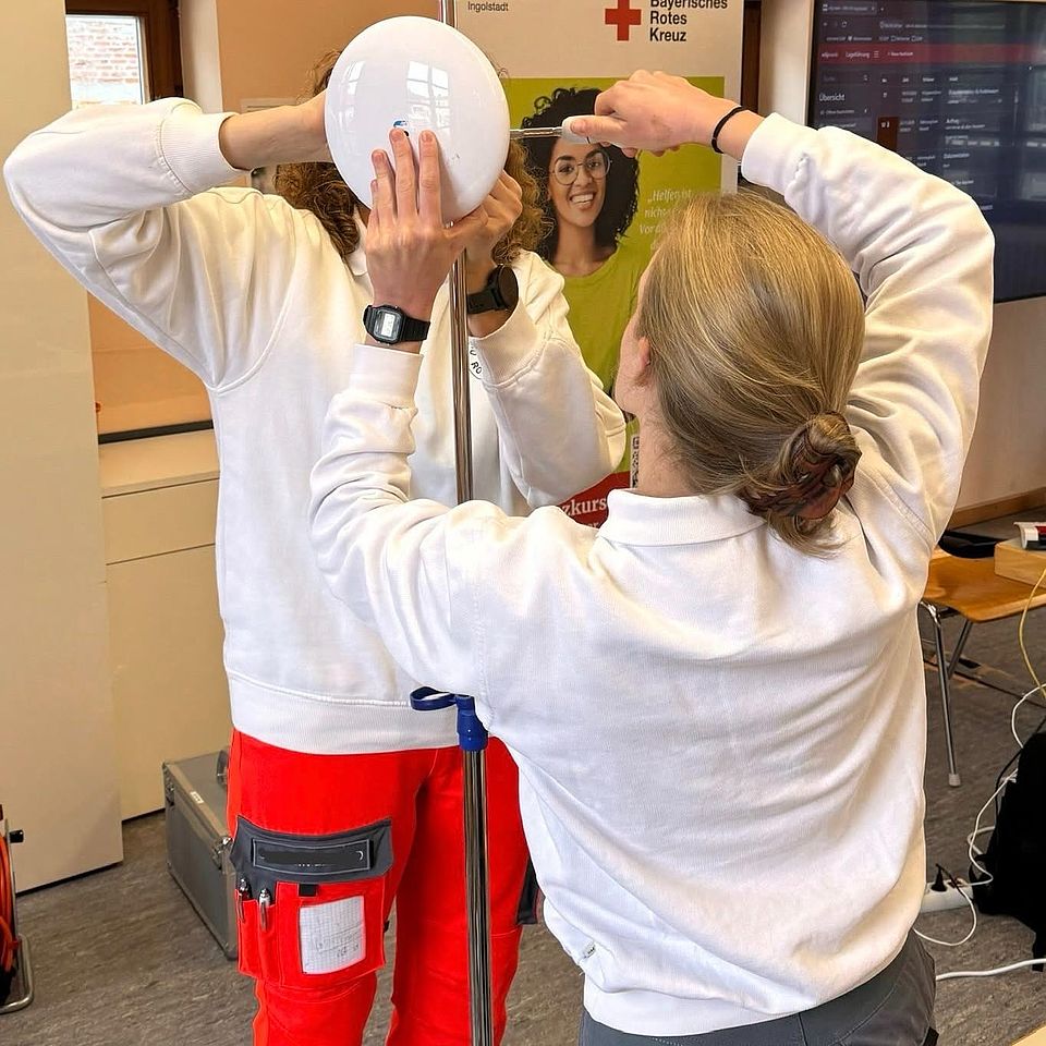 Das Foto zeigt eine uniformierte Frau und einen uniformierten Mann, die zu Übungszwecken eine weiße runde Scheibe an eine Stange montieren.