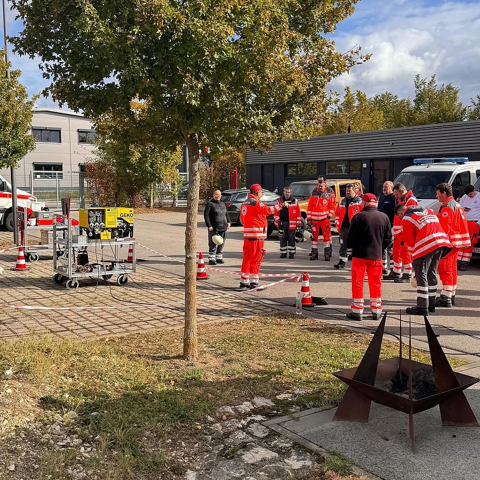 Das Foto zeigt den Außenbereich des BRK-Katastrophenschutzzentrums. Im Bild sind rund ein Dutzend Einsatzkräfte in Uniform.